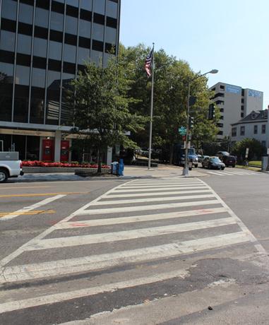 Illustration of what a pedestrian might see as he or she attempts to cross from the west side of Connecticut Avenue Northwest to the east side of the street along Van Ness Street Northwest. The photograph is taken from the pedestrian perspective. Traffic travelling parallel to the pedestrian is waiting for a traffic signal phase change.