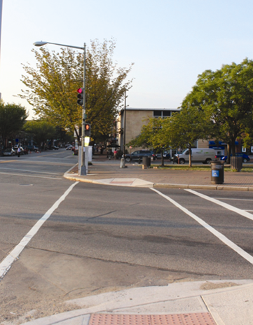 Illustration of what a pedestrian might see as he or she attempts to cross from the south side of Pennsylvania Avenue Southeast to the north side of the street along 8th Street Southeast. The photograph is taken from the pedestrian perspective. A grassy area can be seen on the opposite side of the roadway. No other pedestrian traffic is present. 