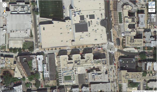 Aerial view of location 18. The solid red rectangle highlights the intersection of 14th and Irving Streets Northwest. The dotted red rectangle highlights the intersection of Irving Street and Hiatt Place Northwest in Washington, DC. Researchers recorded pedestrians crossing north/south on Irving Street between 14th Street and Hiatt Place. The aerial view reveals mostly commercial buildings with a football field belonging to a nearby school. 