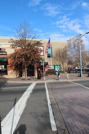 Illustration of what a pedestrian might see as he or she attempts to cross from the south side to the north side of Clarendon Boulevard along North Edgewood Street in Arlington, VA. The photograph is taken from the pedestrian perspective, and a pedestrian can be seen waiting to cross the roadway.