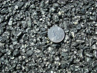 The photo shows a quarter resting on a black asphalt  pavement surface with pores in the asphalt visible.