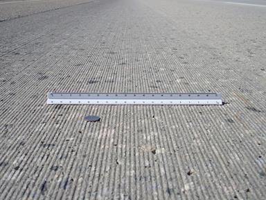 This photo was taken looking down  the length of a concrete road with longitudinal ridges. A coin and scale are  shown for reference.