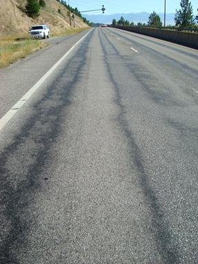 The photo was taken looking down the length  of a road. The left and right wheelpaths in both lanes are dark, lined by black.