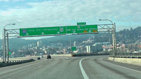 The photo shows an exit ramp off of a highway. Two signs hanging above the road span both the highway and the exit ramp. One sign has three directional arrows pointing to the highway, and one sign has two directional arrows pointing to the exit ramp.