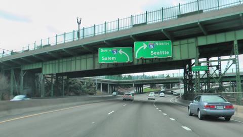 The photo shows vehicles on a highway that is about to curve slightly to the right. Hanging from a bridge above the highway are two signs, with a destination name and a curved arrow pointing left, and one with a destination name and a curved arrow pointing right. Neither sign is pointing to an exit ramp off of the highway.