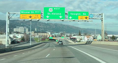 This photo shows a highway with a right-hand exit ramp a small distance away and direction signs hanging above. The ramp appears to dip and bend as it leaves the highway, and at that spot where the photo has been taken, the arrows on the direction signs appear not to match their lane assignments.