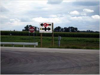 Figure 1. Photo. CICAS-SSA (DII) prototype implemented by Minnesota. This photo features a digital billboard displaying Cooperative Intersection Collision Avoidance System—Stop Sign Assist alerts. The billboard shows a yellow bar when another vehicle is present on the cross street, and a red bar with a do-not-turn symbol when an approaching vehicle is close enough to the intersection for the turn to be unsafe.