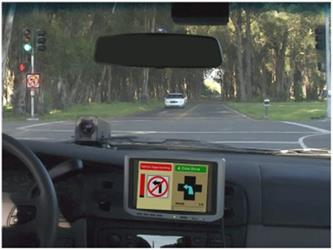 Figure 2. Photo. CICAS-SLTA implemented at a signalized intersection. This photo features alert messages displayed by the Cooperative Intersection Collision Avoidance System—Signalized Left Turn Assist application driver-vehicle interface and driver-infrastructure interface displays. The photo shows a forward driver-side view of a signalized intersection with an oncoming vehicle approaching with the right of way. A dynamic sign external to the vehicle displays a left-turn-prohibited sign. An in-vehicle display shows the same message.