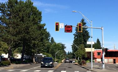 Figure 3. Photo. Example of a CICAS-V DII. Adapted from previous research implementation. This photo features an alert message used to provide Cooperative Intersection Collision Avoidance System to prevent Violations warning on driver-infrastructure interface. The photo shows a driver’s view of an intersection. Two post-mounted traffic signals displaying the red phase can be seen. In between these signals is a square digital display showing the Cooperative Intersection Collision Avoidance System to Prevent Violations driver-infrastructure interface, which consists of a stop-sign icon with a red outline.