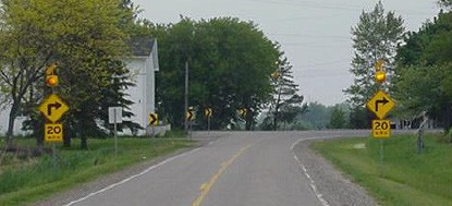 Figure 173. Photo. Curve warning sign and chevron sign and flashing beacons.  This figure shows an example of a curve warning sign and a chevron sign and flashing beacons. Curve warnings signs are placed on the approach to a horizontal curve. These are supplemented with flashing beacons to attract the driverâ€™s attention and chevrons to delineate the curve.