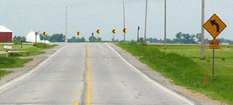 Figure 174. Photo. Curve warning sign and chevron sign. This figure shows an example of a curve warning sign and a chevron sign. Curve warnings signs are placed on the approach to a horizontal curve. These are supplemented with chevrons placed along the curve.