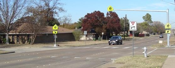 Figure 2. Photo. Study site from TxDOT study showing overhead RRFB installation. A pedestrian crosswalk that is supplemented by rectangular rapid flashing beacons. One set of post-mounted beacons is on each side of the road, and one set is above the center of the road on a mast arm.