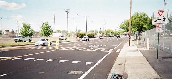Figure 5. Photo. Unsignalized pedestrian crosswalk in Folsom, CA. The midblock crosswalk is marked with a ladder design and crosses a roadway with four through lanes and a two-way left-turn lane. A triangle yield line is marked on the pavement in advance of the crosswalk. There is an R1-5 pedestrian crossing sign on the right side of the roadway at the advance yield line and two R1-6 pedestrian delineators in the median.