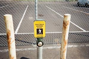 Figure 7. Photo. Unsignalized pedestrian crosswalk in Folsom, CA, pedestrian pushbutton. The pedestrian pushbutton is located near the top of a short pole. Above the push button is a yellow plaque that reads “Crosswalk Warning Device: Caution” and has an image of a pedestrian on it.