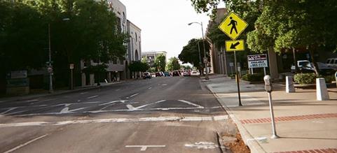 Figure 8. Photo. Unsignalized pedestrian crosswalk in Stockton, CA. The midblock crosswalk is marked with an alternating zig-zag pattern and crosses a one-way roadway with four through lanes and metered parking allowed on the right side of the roadway.