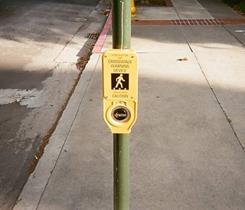 Figure 10. Photo. Unsignalized pedestrian crosswalk in Stockton, CA, pedestrian pushbutton. The pedestrian pushbutton is located on a pole. Above the push button is a yellow plaque that reads “Crosswalk Warning Device: Caution” and has an image of a pedestrian on it.