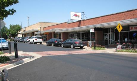 Figure 12. Photo. Unsignalized pedestrian crosswalk in Overland Park, KS. The midblock crosswalk is marked with a solid red color and crosses a two-lane urban roadway with parking on both sides of the road. There are raised bulbouts on either end of the crosswalk to shorten the crossing distance and to make the crosswalk more visible to approaching drivers. A pedestrian crosswalk sign (W11-2) is located on the sidewalk at the crosswalk.