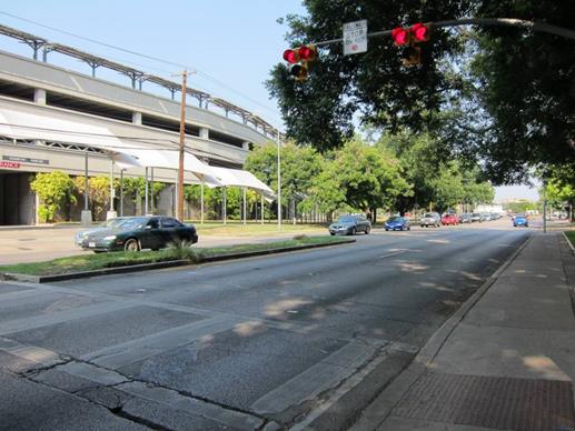 Figure 18. Photo. Crosswalk on Barton Springs Road in Austin, TX. A pedestrian crosswalk on a four-lane divided arterial. The picture shows one half of the crosswalk, as well as the downstream vehicle lanes and the adjacent sidewalk. The crosswalk is controlled by a pair of mast-arm mounted pedestrian hybrid beacons, which are shown in the picture in the solid red phase. A “PEDESTRIANS STOP ON RED” sign is mounted on the mast arm between the two beacons.