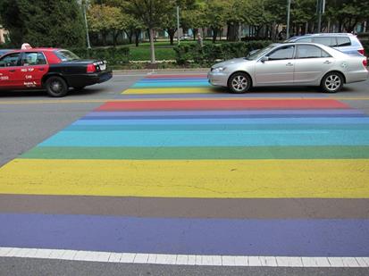 Figure 20. Photo. Colored pavement markings used to promote local area. The color stripes look like an unsignalized midblock pedestrian crosswalk in Arlington, VA. The stripes are of various widths. The road is two-way with two through lanes in each direction. There are no pedestrians crossing the roadway, but the vehicle queue from an adjacent signal has backed up over the markings.