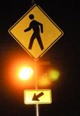 Figure 25. Photo. C-B12, lap A study assembly. A Pedestrian Crossing sign assembly with a set of 12-inch circular beacons between the W11-2 sign and the W16-7P arrow plaque, shown at night.