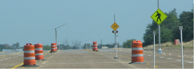Figure 41. Photo. View of discomfort glare course. A drivers-view image of the road course constructed for the discomfort glare study. The road is bounded by orange-and-white work zone barrels on each side. The two sign assemblies are installed 15 ft to the right of the right edge of the road, 0.2 mi apart. The sign nearest to the driver is the Pedestrian Crossing sign shown in figure 40; the second sign is the experimental diamond-shaped sign shown in figure 39. Some barrels on the right side of the road have been replaced by delineators to indicate the locations where subject drivers will be asked to evaluate the signs.