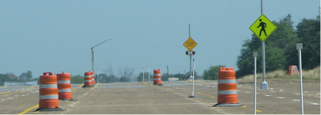 Figure 41. Photo. View of discomfort glare course. A drivers-view image of the road course constructed for the discomfort glare study. The road is bounded by orange-and-white work zone barrels on each side. The two sign assemblies are installed 15 ft to the right of the right edge of the road, 0.2 mi apart. The sign nearest to the driver is the Pedestrian Crossing sign shown in figure 40; the second sign is the experimental diamond-shaped sign shown in figure 39. Some barrels on the right side of the road have been replaced by delineators to indicate the locations where subject drivers will be asked to evaluate the signs. Figure 41. Photo. View of discomfort glare course. A drivers-view image of the road course constructed for the discomfort glare study. The road is bounded by orange-and-white work zone barrels on each side. The two sign assemblies are installed 15 ft to the right of the right edge of the road, 0.2 mi apart. The sign nearest to the driver is the Pedestrian Crossing sign shown in figure 40; the second sign is the experimental diamond-shaped sign shown in figure 39. Some barrels on the right side of the road have been replaced by delineators to indicate the locations where subject drivers will be asked to evaluate the signs.