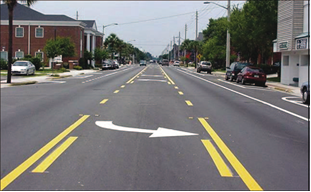 Figure 105. Photo. Three-lane configuration after road diet. The same street as shown in figure91, but it has a three-lane cross section with one travel lane in each direction and a two-way left-turn lane in the center. Bicycle lanes and marked spaces for on-street parking are also provided on each side of the street.