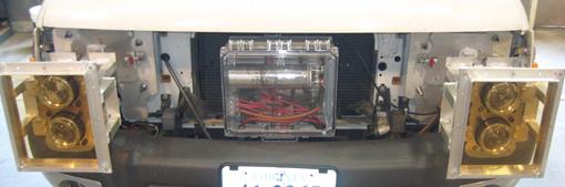 Figure 25. Photo. Test vehicle with headlamps and interchangeable gels. The photo shows the front of the test vehicle with two sets of two 90-mm (3.9-inch) Hella® Bi-Xenon high-intensity discharge projector headlamps. The box in the center contains a 1-F capacitor to stabilize headlamp input voltage. In front of the headlamps are square brackets in which yellow transmittance filter gels are mounted. 