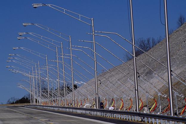 Figure 73. Photo. MPI system performance experiment—visual clutter on the Smart Road. The photo shows a guard rail, a section of roadway, and a steep hill on the shoulder. It also shows a number of overhead lighting masts and rain towers.