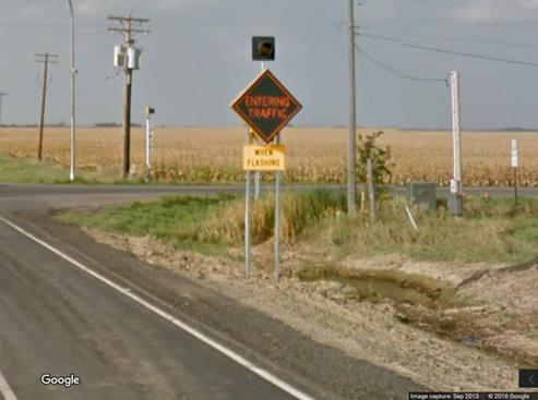 Figure 8. Photo. Major route blank-out sign with flashing beacon from Google Street ViewTM. This photograph shows a post-mounted blank-out sign on a major road displaying the "ENTERING TRAFFIC" message, "WHEN FLASHING" plaque, and one flashing beacon.