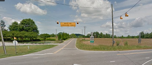 Figure 15. Photo. Minor route overhead static sign with flashing beacons from Google Street ViewTM. This photograph shows an overhead warning sign on minor road stating "WATCH FOR APPROACHING VEHICLE" with two flashing beacons. There are two flashing beacons on the major road approach.