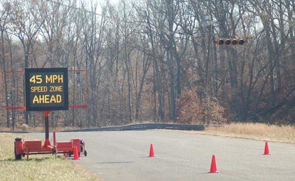 Figure 41. Photo. The CMS used in the study. This figure shows an example of the changeable message sign (CMS) used in the study. The CMS is mounted on a trailer on the left side of the road. There are three cones the roadway.