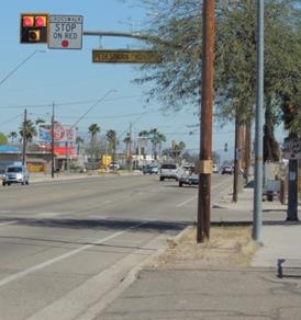Figure 53. Photo. Example of PHB installation in Tucson, AZ. This photo shows a pedestrian hybrid beacon (PHB) at a crosswalk in Tucson, AZ. The beacon is mounted on a mast arm, and the face of the beacon is composed of two red signal indications side by side and one yellow signal indication centered below the red signal indications. The signals are placed on a black back plate with a yellow border. The mast arm also has a R10-23 STOP ON RED regulatory sign next to the beacon and an illuminated pedestrian crossing sign hanging from the mast arm.