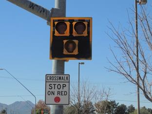 Figure 55. Photo. Example of sign used in Tucson, AZ. This photo shows a pedestrian hybrid beacon mounted on a signal pole in Tucson, AZ. The face of the beacon is composed of two red signal indications side by side and one yellow signal indication centered below the red signals. The signals are placed on a black back plate with a yellow border. Below the beacon there is a R10-23 crosswalk stop on red sign.