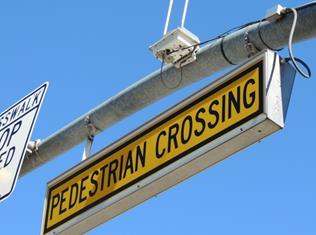 Figure 56. Photo. Example of internally illuminated sign used in Tucson, AZ. This photo shows a yellow sign hanging from the mast arm. The sign has a yellow background with a black border that reads, "Pedestrian Crossing" in black letters.