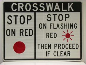Figure 57. Photo. Sign used in Austin, TX. This photo shows a STOP ON RED sign used in Austin, TX. The sign is a rectangle with a white retroreflective background and a black border. The top part of the sign is black with "CROSSWALK" in white letters. Below that there are two boxes. The box on the left reads "STOP ON RED" in black letters with a red circle below the lettering. The right box reads "STOP ON FLASHING RED THEN PROCEED IF CLEAR."