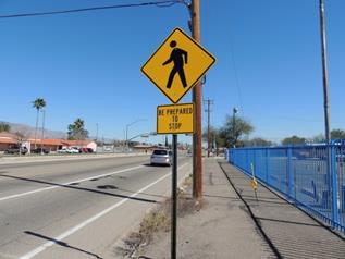 Figure 59. Photo. Example of advance warning sign used in Tucson, AZ. This photo shows a W11-2 pedestrian crossing warning sign mounted on a post. Below the sign there is a rectangular plaque with a yellow background and a black border. In black lettering it reads "BE PREPARED TO STOP."