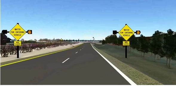Figure 4. Screenshot. ICWS signs on four-lane divided highway approach. This screenshot features one-half (two lanes) of a four-lane divided highway. There are identical intersection conflict warning system setups on both sides of the lanes. The setups include a yellow diamond sign that reads, “WATCH FOR ENTERING VEHICLE,” beacons on both sides of the diamond sign (one of which is lit), and a square yellow placard below the diamond sign that reads, “WHEN FLASHING.”