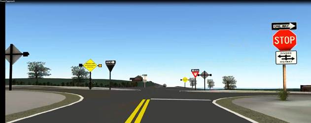 Figure 22. Screenshot. Exemplar from video showing the ICWS sign placement across from the stop and yield lines. This screenshot features a minor road intersecting with a four-lane divided highway and is situated from the perspective of the minor road. On the right side of the intersection is a stop sign, a one-way sign (pointing right), and a square placard that reads, “DIVIDED HIGHWAY,” with arrows indicating the layout of the intersection. On the left side of the dividing media, there is a one-way sign (pointing right) and an intersection conflict warning system (ICWS) with a yellow diamond sign that reads, “WATCH FOR APPROACHING TRAFFIC,” that has beacons on both sides (one of which is lit). On the right side of the dividing media, there is a triangular yield sign and a one-way sign pointing left. On the right corner of the far side of the intersection, there is an ICWS with a yellow diamond sign that reads “WATCH FOR APPROACHING TRAFFIC,” that has beacons on both sides (one of which is lit).