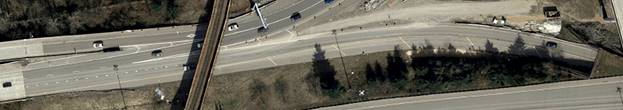 Photo. Overhead view of entering ramp (lower right of image) with asymmetrical widening to the left in a left-hand horizontal curve. At its far left, this photo shows a freeway-to-freeway ramp emerging from a tunnel in a left-hand curve. To the left is a left-hand auxiliary lane, which serves as a deceleration lane for a left-hand exit from a collector–distributor roadway.