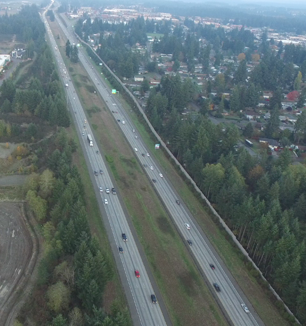 Photo. Example video still from an unmanned aerial vehicle (UAV) at site 43-3. This UAV photo consists of three lanes. A fourth lane is added with the rightmost lane an exit-only lane, and the adjacent lane an option lane. Three attributes are present: auxiliary lanes—attribute 4110; exit with downstream split—attribute 4222; and guide signs for option lanes—attribute 5130.