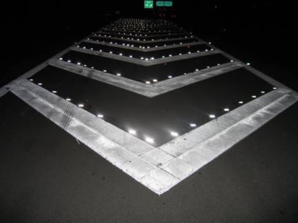 Photo. Gore area markings on a freeway in South Carolina. This night-time photo shows gore area markings that combine well-maintained, plastic-type markings of sufficient width to be visible as transverse markings with raised reflective pavement markers.