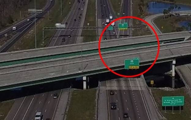 Photo. Use of multiple signs approaching a single departure point. This aerial photo depicts how an overcrossing roadway obscures the view of two exit direction signs in the gore area, while the upstream location of a third sign is too far in advance for placement of an exit direction sign. In figure 77, the obscured signs are identified in a superimposed red circle.