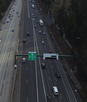 Photo. Use of a tapered lane addition to enter the general-purpose lanes of a freeway from the managed lanes. This aerial photo shows access to general-purpose freeway lanes from managed lanes by an exiting maneuver that involves a tapered lane addition. A guide sign on the left includes an angled-up arrow placed roughly in alignment with the beginning of the exiting movement taper.