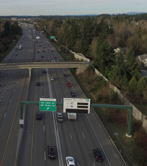 Photo. Use of misleading signing and parallel lanes and lane changes to access the general-purpose lanes of a freeway from the managed lanes. This aerial photo shows a freeway configuration that does not include the addition of a lane or an exit-type maneuver. The access point for the general-purpose lanes is parallel lanes and lane changes, not an exiting maneuver. Motorists are required to access general-purpose lanes from the managed lane. In a guide sign, an angled-up arrow indicates a lane-change movement far ahead of the break in the double-white lines, which prohibits these movements.