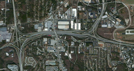 Photo. Aerial view of location 6. This aerial photo shows an interchange that provides complete separation of mainline traffic for two interstates while facilitating all connections between the two routes, serving three intersecting freeway corridors. The quad-carriageway design also provides full access to an embedded service interchange. The interchange uses a somewhat conventional loop-ramp design.