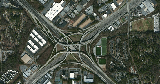 Photo. Aerial view of location 8. This aerial photo shows an interchange typical of four-level interchange design with high-volume connections between the intersecting freeways, including option lanes on the mainline access to the ramps and on ramps at the splits for the two directions of the interstate.
