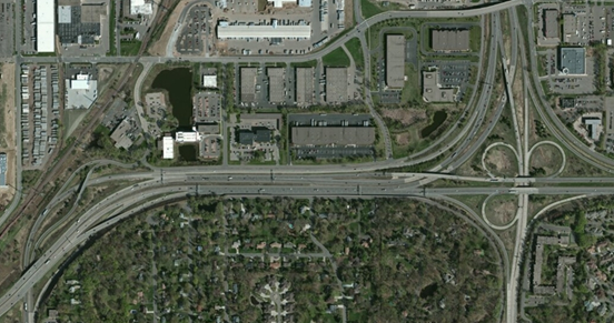 Photo. Aerial view of location 10. This aerial photo shows an interchange with access to a local roadway from the southbound interstate in two locations because of the unseparated entrance lane from the westbound highway to the southbound interstate. A similar braided geometry occurs in the northbound direction, effectively providing two carriageways for the interstate northbound through traffic.