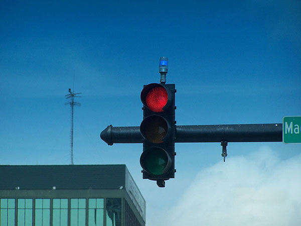 This photo shows a red-light indicator light mounted on a signal head. The bulb connected to the top of the signal head with a support. The signal is in the red phase and the red-light indicator light is activated.