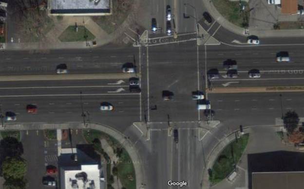 Aerial view of a four-leg urban intersection with driveway entrances on all approach and receiving corners of the intersection. These entrances demonstrate limited corner clearance due to their proximity to the intersection.